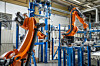 Oransje industrikroboter arbeider i en moderne fabrikkhall.