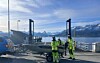Tre personer i refleksklær står ved en båt og en ferjekai med fjell og fjord i bakgrunnen.