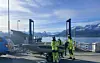 Tre personer i refleksklær står ved en båt og en ferjekai med fjell og fjord i bakgrunnen.