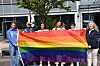 Flere personer står utendørs og holder et stort regnbueflagg foran en bygning.