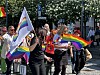 Flere personer går i en gate med regnbueflagg og prideflagg under en markering.