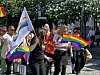Flere personer går i en gate med regnbueflagg og prideflagg under en markering.