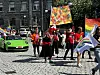 Deltakere i en Pride-parade går i en gate med regnbueflagg og fargerike bannere.