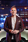 En mann i dress står foran en opplyst bakgrunn i et TV-studio.