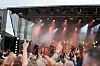 Publikum med hendene i været foran en opplyst utendørsscene med artister.