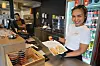 En kvinne i hvit skjorte holder et brett med vårruller foran en disk i et takeaway-lokale.
