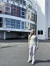 En kvinne står på asfalt foran en hvit bygning med store vinduer og skiltet «AKADEMIET».