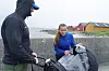 To personer står ved en molo med en trillebag og routstyr foran sjøen.