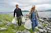 To personer går på en steinete strand med søppelsekker i hendene.