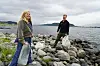 To personer står på en steinete strand og holder søppelsekker ved vannkanten.