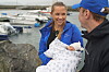 En kvinne og en mann står ved en båthavn og ser på en sovende baby i et teppe.