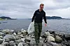 Mann går over steiner ved sjøen og bærer en sekk med søppel.