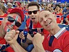 Tre norske supportere sitter tett sammen på en stadion og jubler med rødt og blått ansiktsmaling.