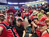 En gruppe supportere i røde og hvite klær tar en selfie på en fullsatt stadiontribune.