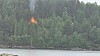 Flammer fra en hytte i skogkledd terreng ved vannet.