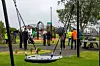 Lekeplass med karusell, sklier og flere voksne og barn i et grønt uteområde.