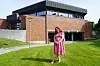 En kvinne i rosa kjole står på en grønn plen foran en moderne mursteinsbygning.