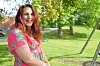 Kvinne med rødt hår og rosa kjole sitter utendørs i en park med trær og gress.