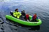 Fire barn sitter i en grønn gummibåt på vannet, med en voksen bak ved motoren.