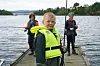 Tre barn står på en brygge ved vannet med fiskestenger og redningsvester.