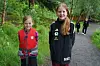 To barn står på en skogssti, den ene med rød redningsvest og den andre i svart sportsdress.