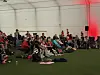 Folk sitter på stoler og tepper i et stort telt og ser på en fotballkamp på storskjerm.