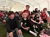Barn og voksne sitter på gulvet i et stort telt og ser på en fotballkamp på skjerm.