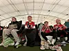 Fire barn sitter på stoler i et telt, kledd i rødt og svart og holder norske flagg.