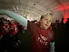 Barn i røde fotballtrøyer står i et lokale og ser mot en stor skjerm utenfor bildet.