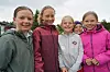 Fem barn i regnjakker står tett sammen utendørs og smiler mot kamera.