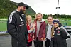 Fire barn og en trener står samlet på en fotballbane og smiler mot kamera.