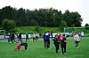 Barn og voksne står samlet på en fotballbane med mål i bakgrunnen.