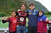 Fire personer står sammen på en fotballbane med fjell i bakgrunnen, tre av dem i fotballdrakter.
