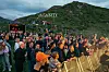 Stor folkemengde står foran en utendørsscene ved et fjell i skumringen.