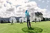 Flere personer står i gjennomsiktige gående bobler på en grønn gresslette ved et hus.