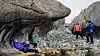 Turgåere ved en stor overhengende steinformasjon i et steinete fjellområde.