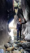 Person med hjelm står på steiner i en smal fjellkløft mellom høye bergvegger.