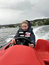 En person kjører en rød fritidsbåt i høy fart på sjøen under overskyet vær.