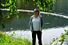 En kvinne står ved en innsjø med trær og gress rundt seg.