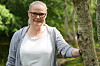 En kvinne med briller står ute i naturen ved et tre og smiler mot kameraet.
