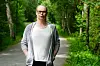 En kvinne går på en smal sti i en grønn skog og ser mot kamera.
