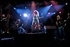 Vokalist synger på scene med band, sterke røde og blå scenelys i bakgrunnen.