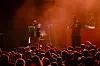Band opptrer på scene foran publikum i rødt lys og røyk.