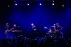 Liveband spiller på scene i blått lys mens publikum ser på i forgrunnen.