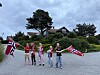 Flere barn står på en vei og vifter med norske flagg foran hus og trær.