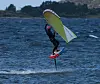 Vingfoil-utøver svever over bølgene med gulgrønn seilvinge og rød foilbrett.