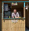Bartender står bak en bambusbar med drikkevarer, dekor og et neonskilt i en liten strandbar.