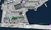 Satellittkart over et havneområde med bygninger, veier og vann langs en kai.