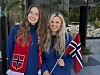 To smilende kvinner står utendørs og holder hvert sitt røde flagg med hvitt og blått kors.