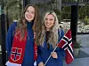 To smilende kvinner står utendørs og holder hvert sitt røde flagg med hvitt og blått kors.